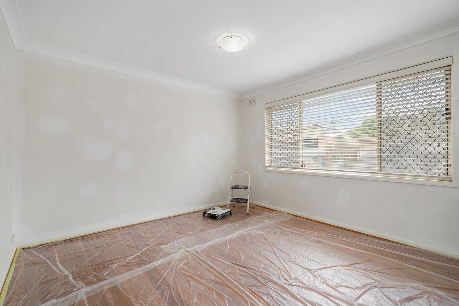 The empty living room of a rental unit with freshly patched walls, a new blind and timber floors.